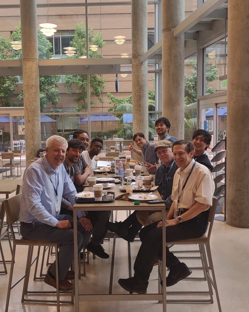 Group of piano technicians sharing breakfast at a long table in the Colburn School atrium after a training session