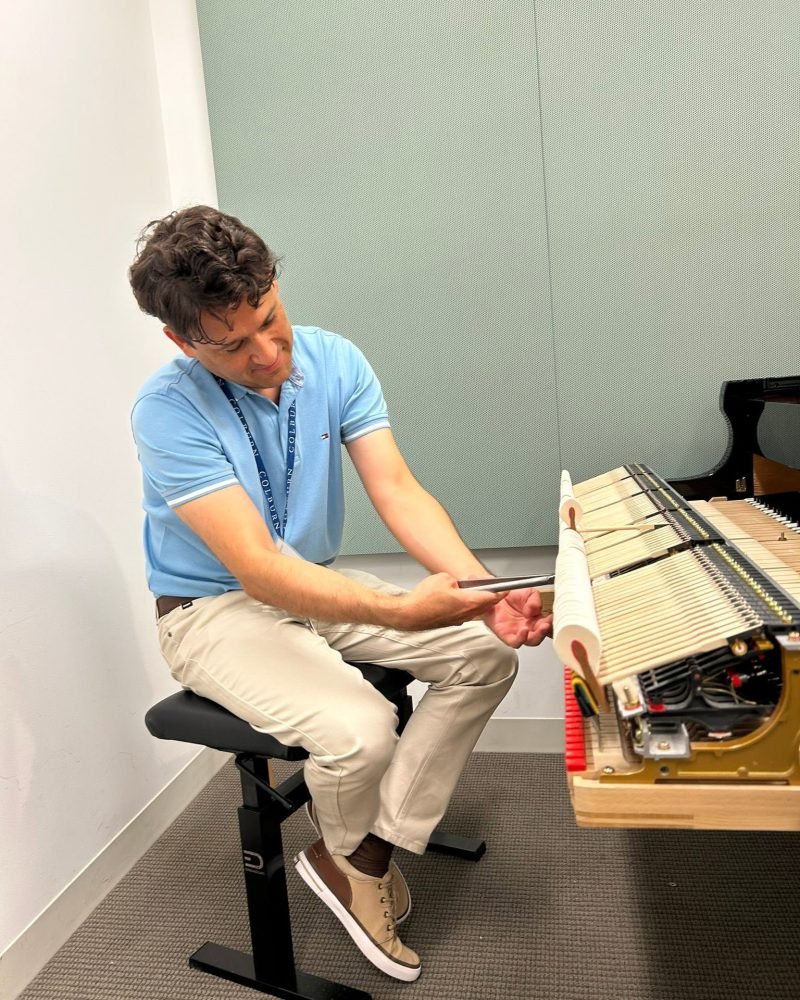 Carlos Boza seated at an adjustable bench, working on a piano action removed from the instrument