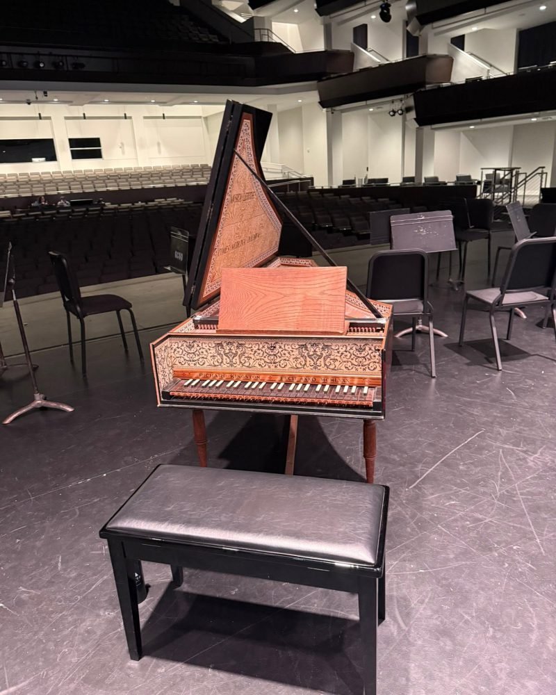 Harpsichord with a painted lid and a bench on an empty concert stage