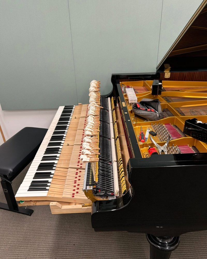 Grand piano with its action pulled out onto the keybed, hammers and dampers exposed, in a practice room