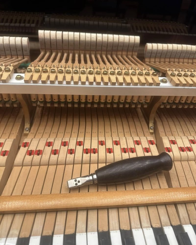 Upright piano action with a tuning lever resting on the keys in front of the hammers