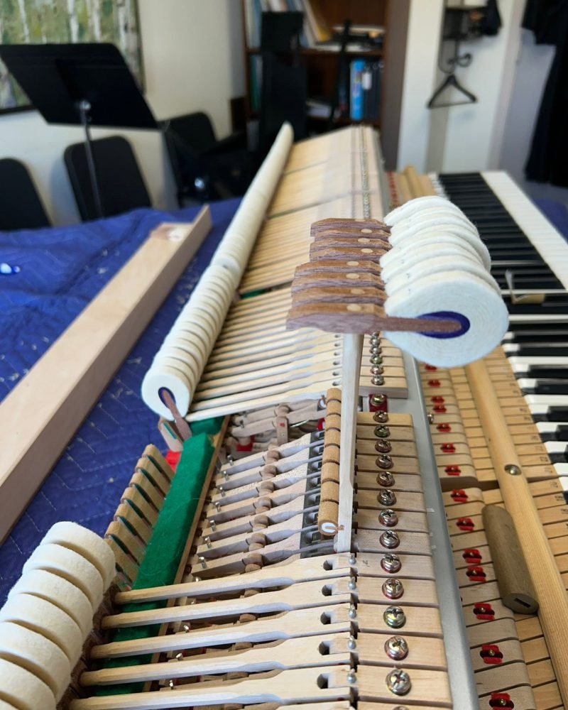 Grand piano action on a padded workbench with several hammers removed for repair