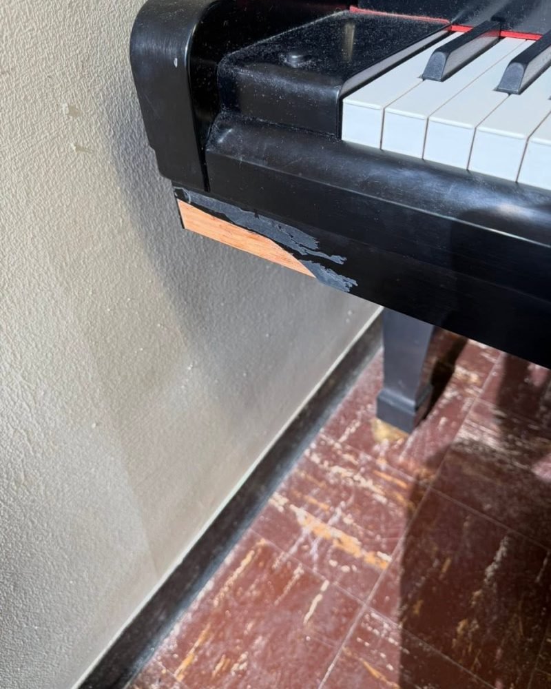 Corner of a black grand piano case after a finish touch-up, the chip no longer visible