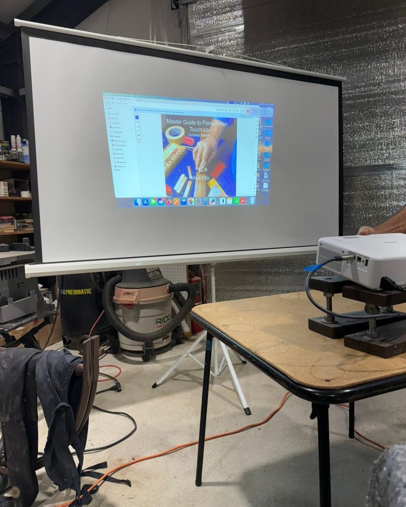 Projector screen in a workshop during a finish touch-up training session, with tools on the table