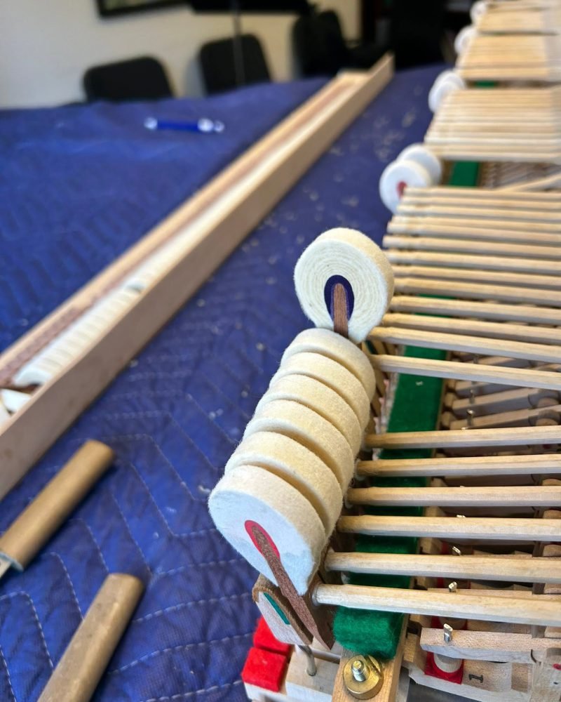 Row of new felt hammers on a piano action rail during restoration, laid on a blue moving blanket