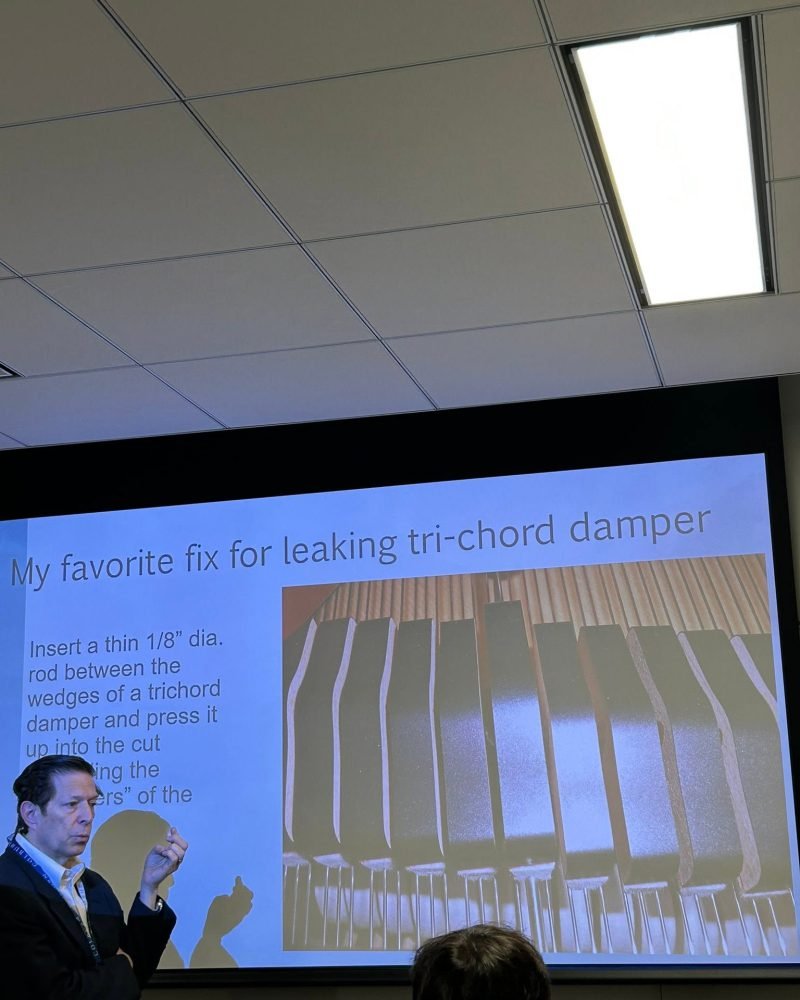 Instructor presenting a slide on fixing a leaking tri-chord damper during a piano technicians seminar