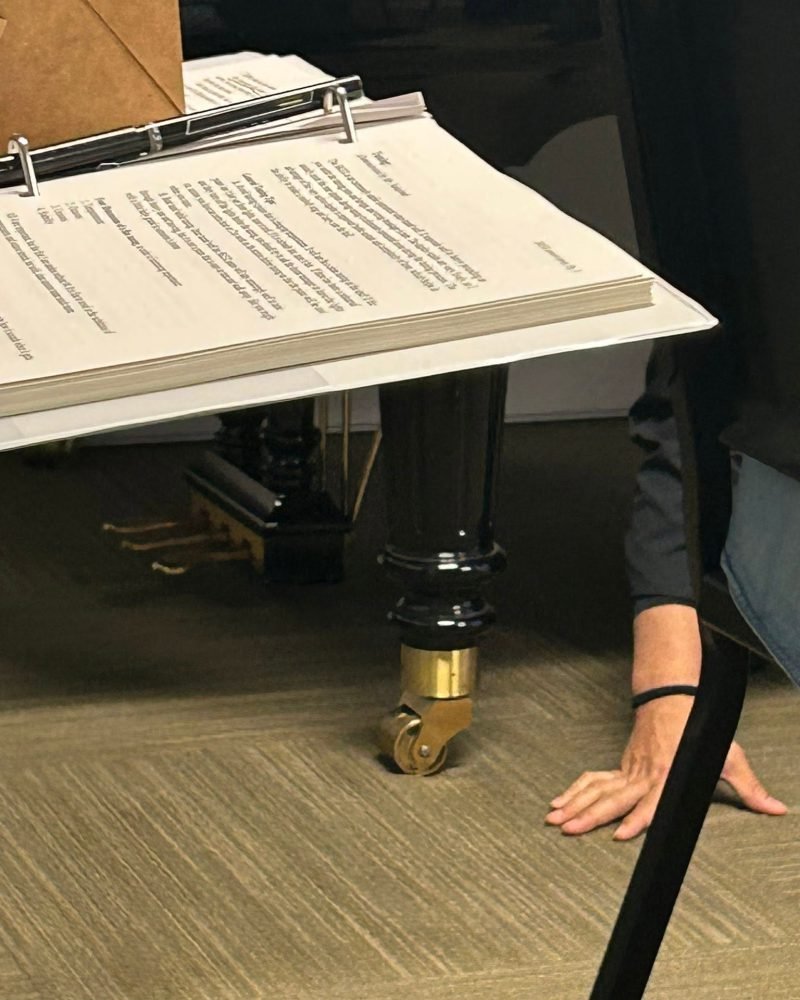 Service notes in a binder beside a grand piano leg and caster during a job
