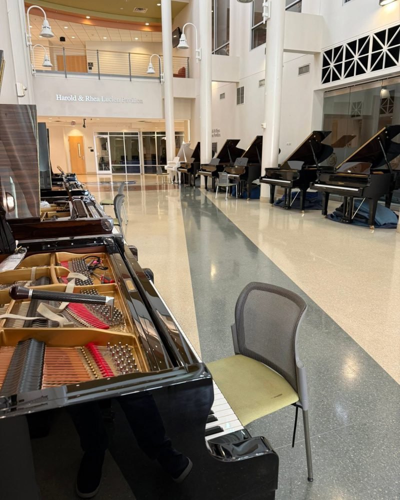 Grand piano with the lid up in a bright lobby, with several other grand pianos along the wall