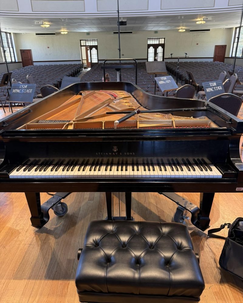 Steinway grand piano and a tufted bench on the stage of the University of Southern Mississippi auditorium, facing empty seats