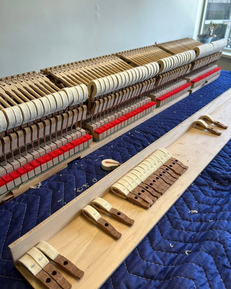 Upright piano action on a blue moving blanket with new hammer parts lined up on a rail for replacement